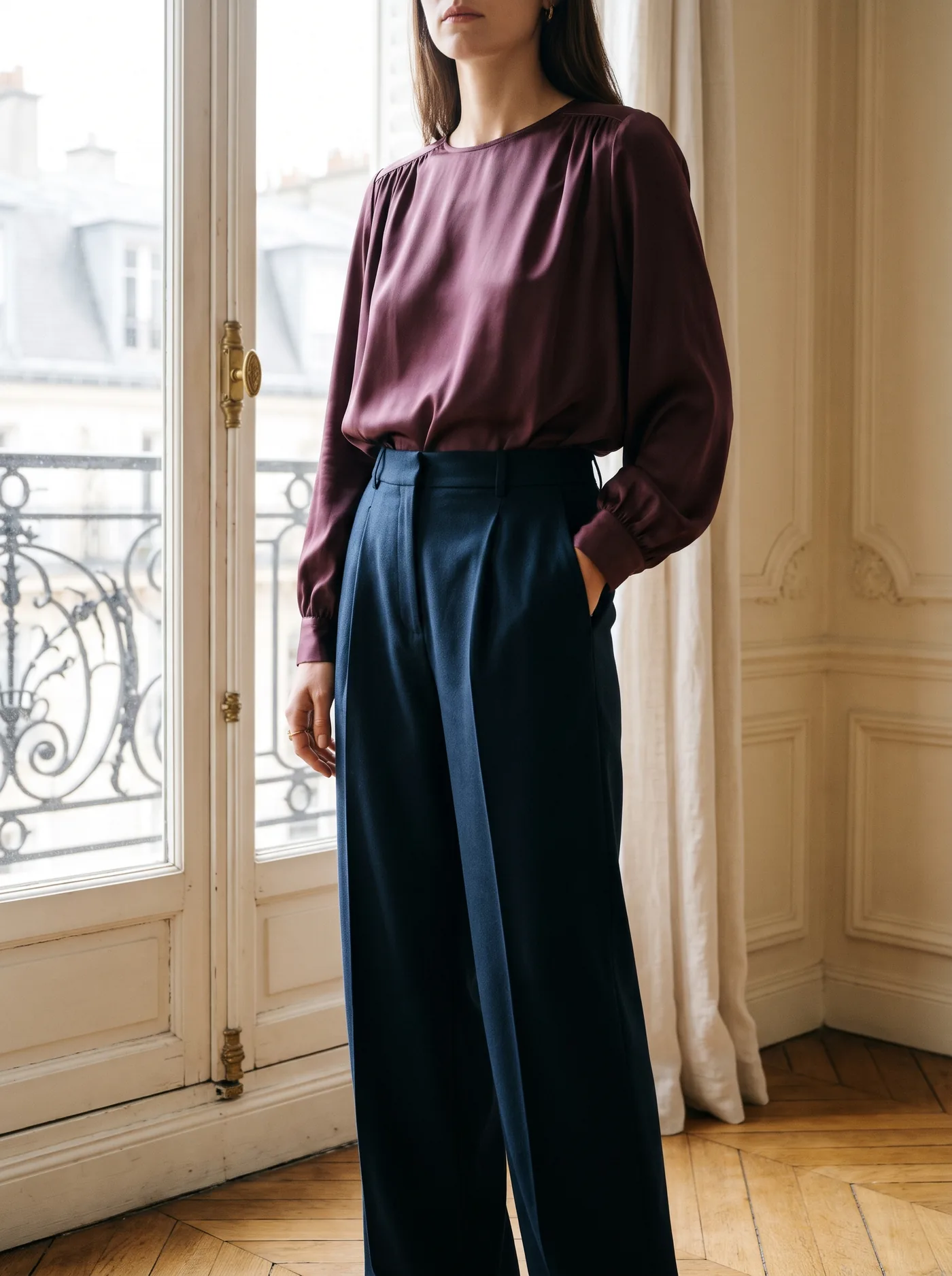 Blouse en satin prune et pantalon large bleu encre devant une fenêtre haussmannienne